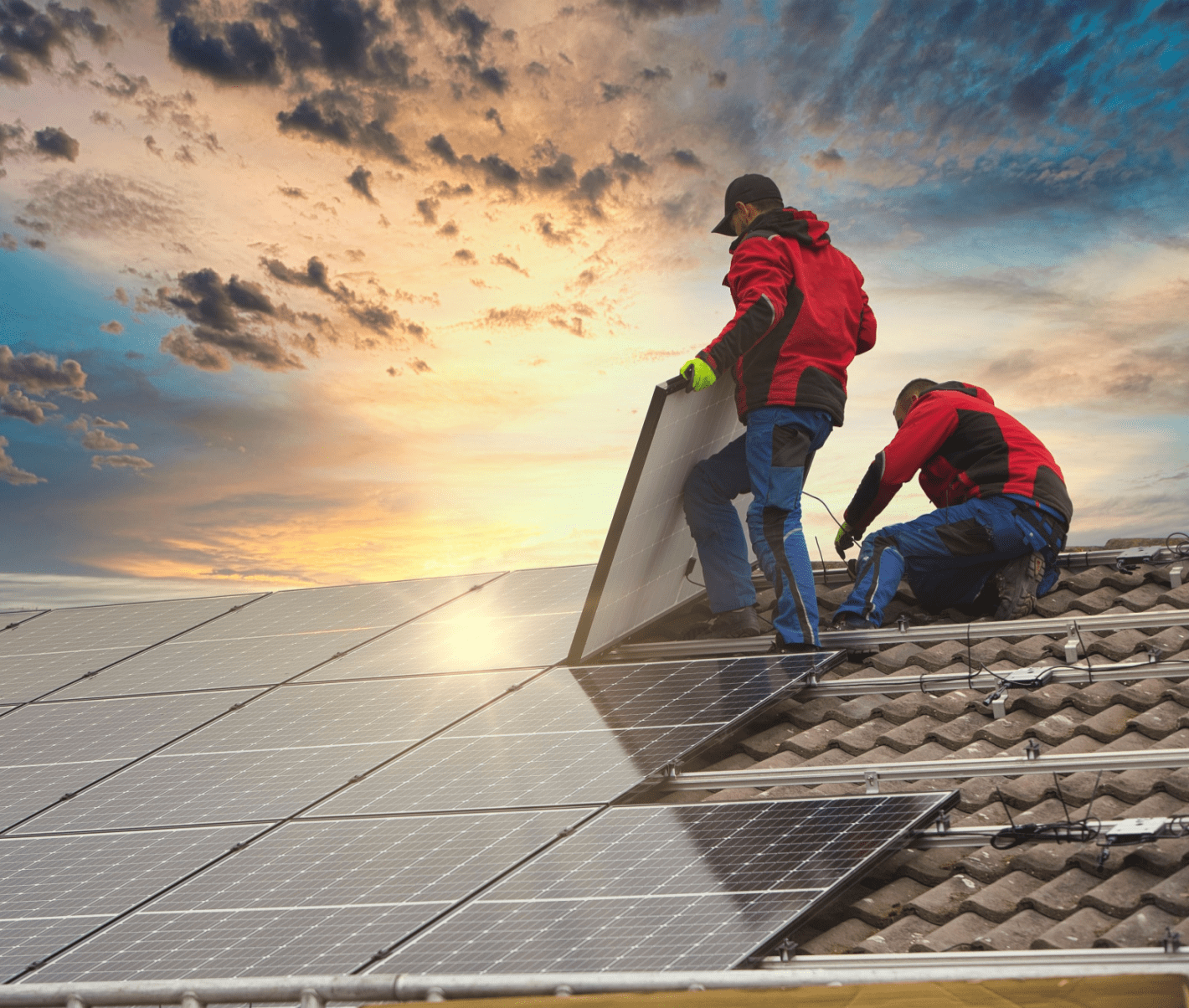 Contractors installing rooftop solar panels during sunset